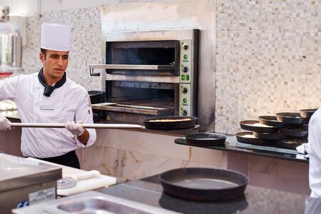 Sharm el sheikh, Egypt - Jyle 28, 2019: Cook took baked pizza from oven in kitchenのeditorial素材