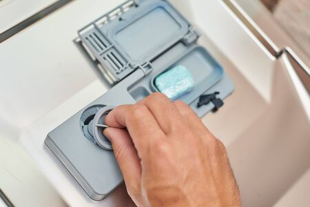 Hand putting soap tablet in dishwasher machine, close up. Kitchen domestic appliance concept