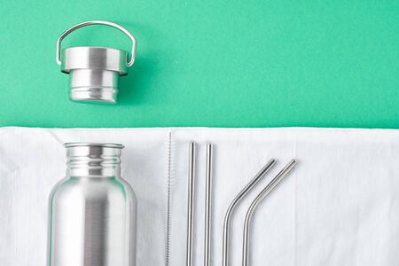 Aluminum bottle, metal tubes and shopping bag on green background. Reusable eco friendly items. Zero waste eco friendly conceptの写真素材