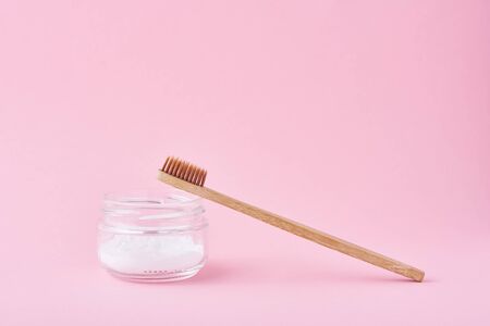 Wooden bamboo toothbrush and baking soda powder in glass jar on pink background.  Teeth health and keep mouth conceptの写真素材