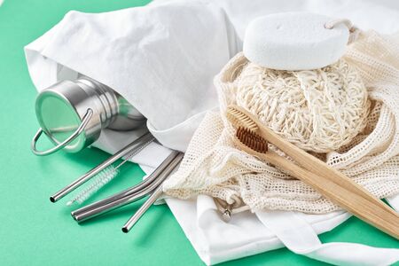 Zero waste concept. Eco friendly reusable items in natural shopping bag. Bamboo toothbrushes, spongle, aluminum bottle and metal tubes on green background.の写真素材