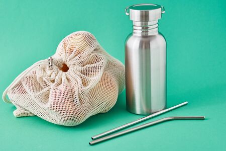 Aluminum bottle , metal tubes and fruits in natural bag on green background. Eco friendly items close up. Zero waste conceptの写真素材