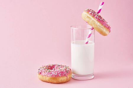 Donuts decorated with icing and sprinkle and glass of milk on pink backgroundの写真素材