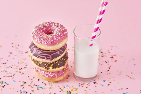 Stack of colorful donuts decorated and glass of milk on pink backgroundの写真素材