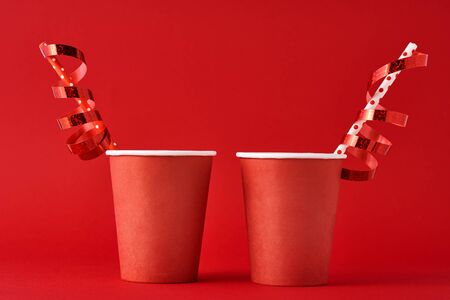 Two paper coffee cups with decorations and straw on red background. Valentines day festive conceptの写真素材