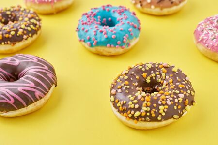 different types of colorful donats decorated sprinkles and icing on yellow background, top view flat layの写真素材