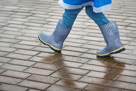 Boy in blue rubber boots walk otdoor in rainy day