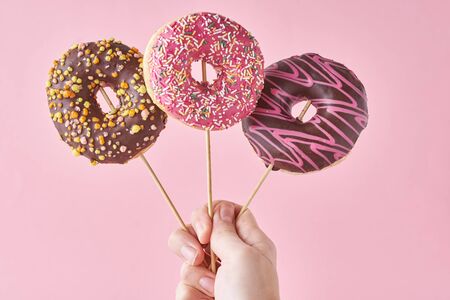 Three donuts in woman hand on pink background. Creative food minimalism styleの写真素材