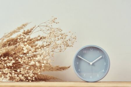 Alarm clock and homemade vase with dries plant on wooden tableの写真素材