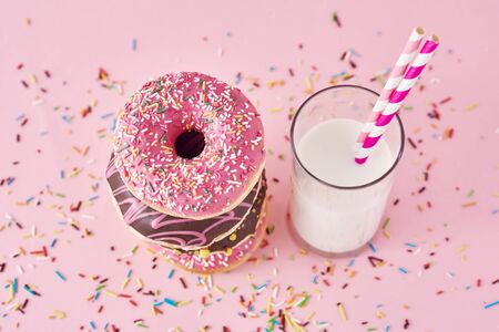 Stack of colorful donuts decorated and glass of milk on pink backgroundの写真素材