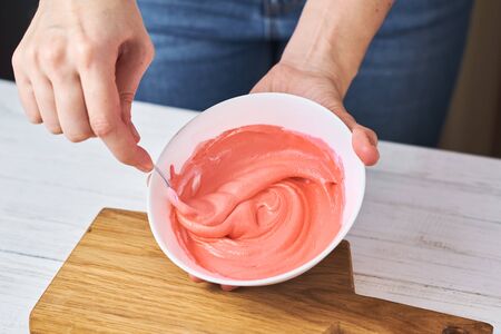 Woman whisking red cream for decorating cookies in bowl on kitchen, closeupの写真素材