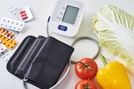 Digital blood pressure monitor, fresh vegetables and medical pills on white background. Healthy...