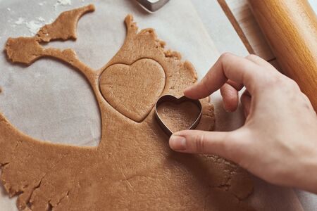 Making gingerbread cookies in shape of a heart for Valentines Day. Woman hand use cookie cutter. Holiday food conceptの写真素材