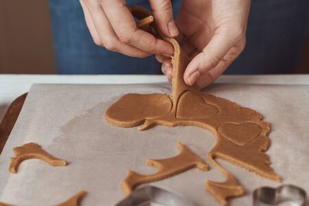 Making gingerbread cookies in shape of a heart for Valentines Day. Woman hand use cookie cutter....