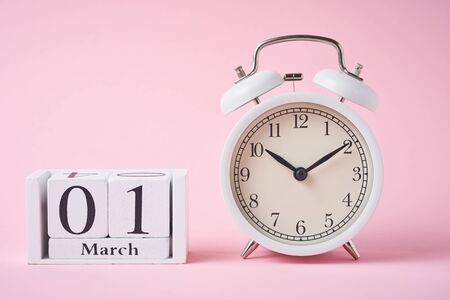 White retro alarm clock with bells and wooden calendar blocks with date 1 march on pink background