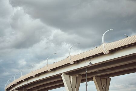 Part of modern bridge with street led lights against cloudy sky. Engineering construction close up