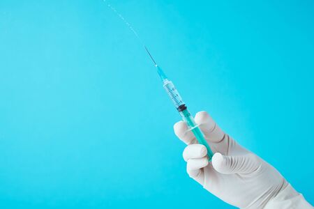 Hands in gloves hold an injection syringe against blue background.  Healthcare, medical and virus...