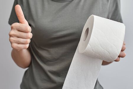 Woman hand hold toilet paper roll and show thumb up gesture, close up. Hygiene conceptの写真素材