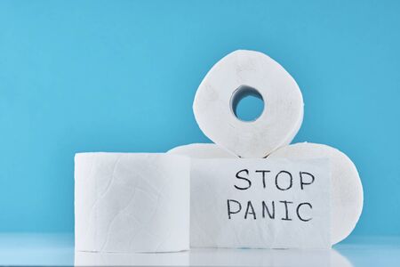 Consumer buying panic about coronavirus covid-19 concept. Toilet paper rolls with inscription stop panic on blue background. People are stocking up essentials for home quarantineの写真素材