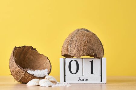 Wooden block calendar with date June 1 and coconut with sea salt on yellow background. Summer vacation conceptの写真素材