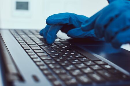 Hand in protective gloves typing on laptop keyboard. Cyber crime and protect information concept