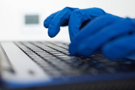 Hand in protective gloves typing on laptop keyboard. Protection from coronavirus covid-19 concept