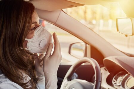 Woman in respiratory mask and medicine gloves driving a car. Protection and self isolation to...