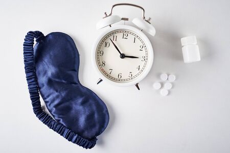 Insomnia, depression and sleeping trouble concept. Alarm clock, sleeping mask and pills on white background, top viewの写真素材