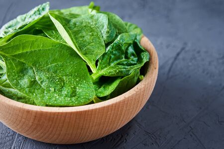 Fresh spinach leaves in wooden bowl on a dark background. Organic foodの写真素材