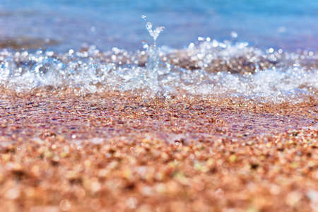 Sea wave on the sand beach, soft focus. Summer background. Waves with splashes and foam.