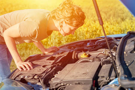 Woman repairs broken car with open hood on the road in summer day 