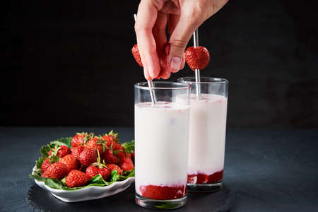 Strawberry milk smoothie in glass with straw and fresh berries on dark backgroundの写真素材