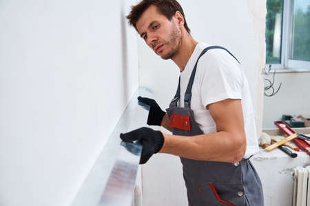 Male worker plastering a wall using a long spatula. Renovation conceptの写真素材