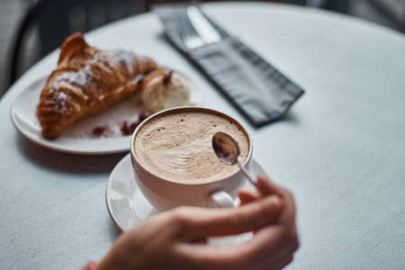 Woman eating breakfast at cafe. Cup of coffee and croissant on a tableの写真素材