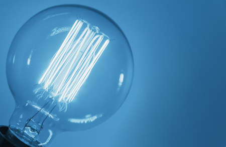 Vintage light bulb on blue background, close up. Glowing edison bulb