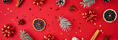 Christmas banner composition. Fir branches, pine cones, dried fruits and festive confetti on red...