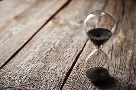 Hourglass on wooden background, close up. Urgency and running out of time concept