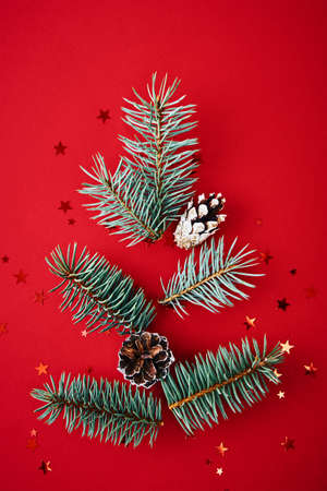 Christmas composition. Fir branches in shape of christmas tree with festive confetti on red backgroundの写真素材