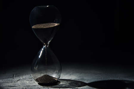 Hourglass on dark background, close up. Urgency and running out of time concept