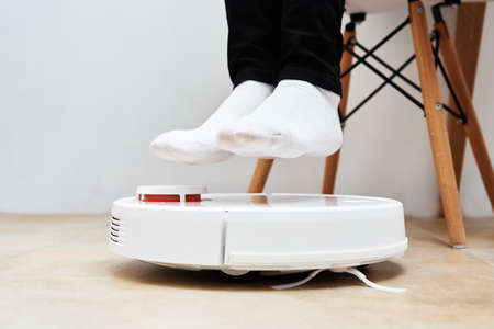 Robot vacuum cleaner working on the floor with furniture, while woman rest. Modern smart householdの写真素材