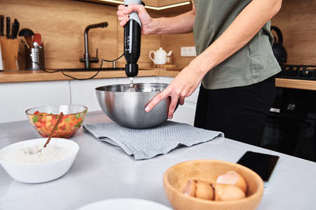 Woman in the kitchen cooking a cake. Hands beat the dough with an electric mixer