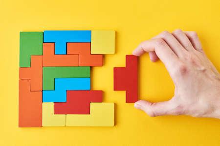 Logical thinking and finishing task concept. Woman hand adding last missing wooden block to finish a puzzleの写真素材