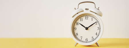 White vintage alarm clock on yellow background, long banner with copy space