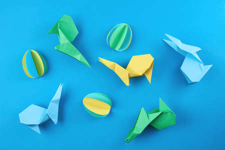 Paper origami Esater rabbits and colored eggs on blue background, top view. Easter celebration...
