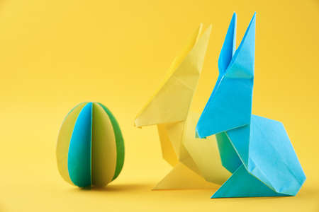 Two paper origami Esater rabbits and colored egg on a yellow background. Easter celebration conceptの写真素材