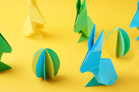 Paper origami Esater rabbits and colored eggs on yellow background, top view. Easter celebration...