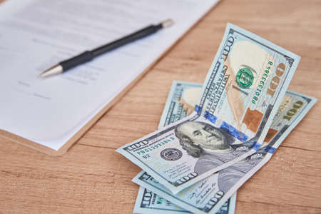 Document, pen and dollar bills on table, close up
