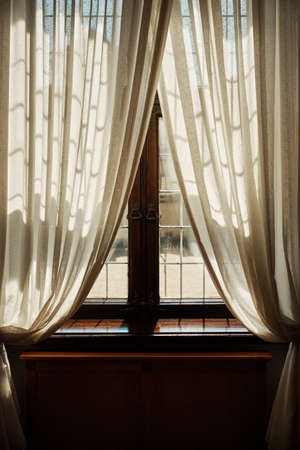 Old window with white curtains and shining rays of the sun