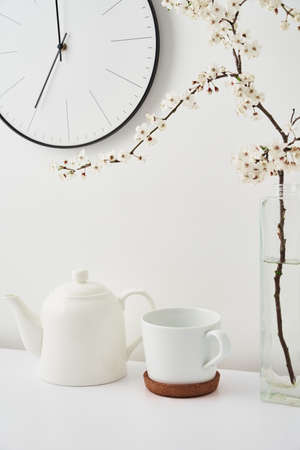 Teapot with cup, plant brunch and wall clock on white background. Minimal style decor concept