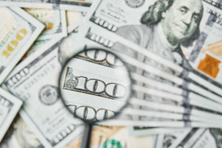 Magnifying glass on dollars bills background. One hundred dollar usd banknotes. Economic and...